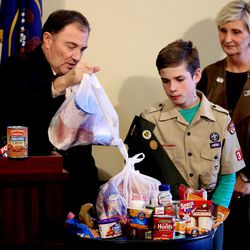 Gov. Gary Herbert adds a bag of perishable food items to a barrel of donations as Boy Scout Ryan Buhler of Taylorsville's Troop 366 and Ginette Bott, chief development officer for the Utah Food Bank, watch at the Capitol in Salt Lake City on Thursday, March 17, 2016.  Residents are encouraged to support Utah Food Bank’s efforts to “Go Green” by filling any bag or box with non-perishable food items and leaving it on their doorstep, which will be picked up by an army of 55,000 Boy Scouts starting at 9 a.m. on Saturday, March 19. 
