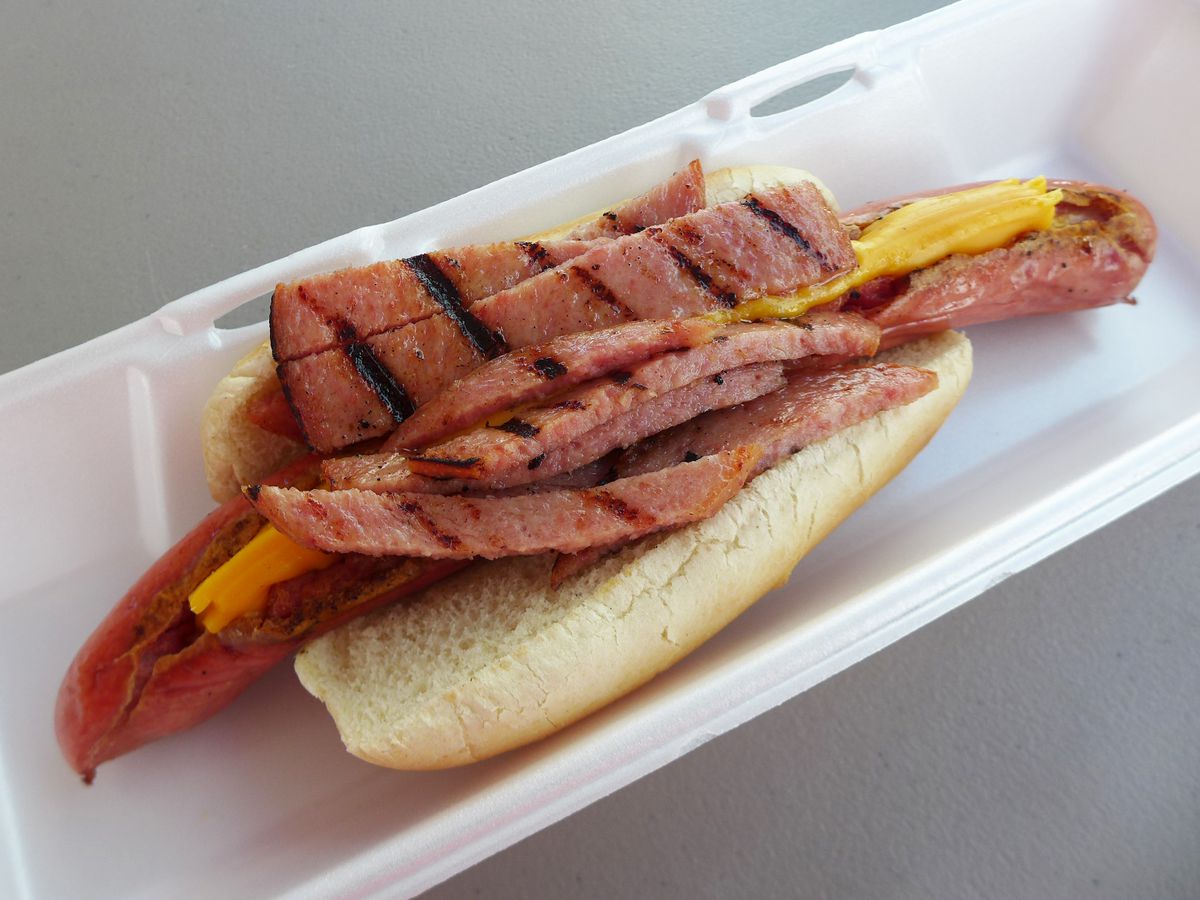A hot dog with cheese in a slit and with luncheon meat heaped on top.