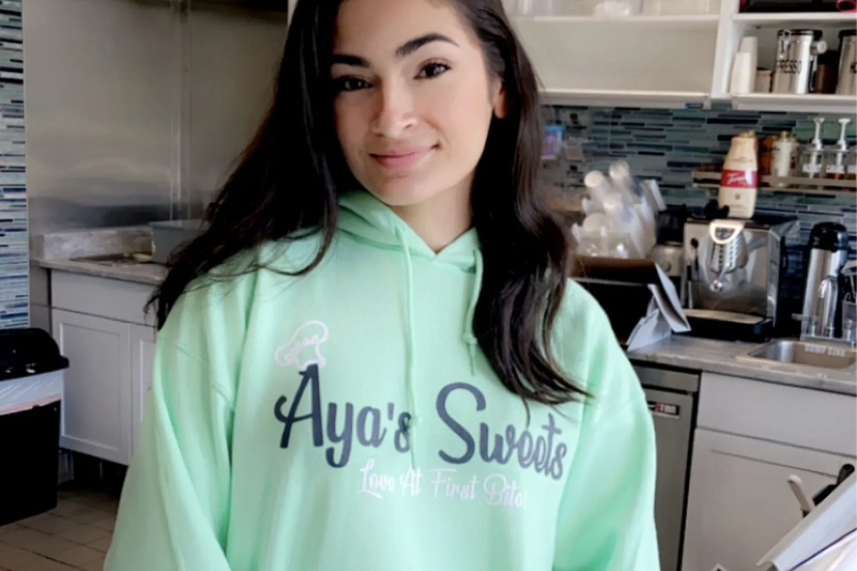 A photo of Aya Islim in the bakery. Her hooded sweatshirt reads Aya’s Sweets