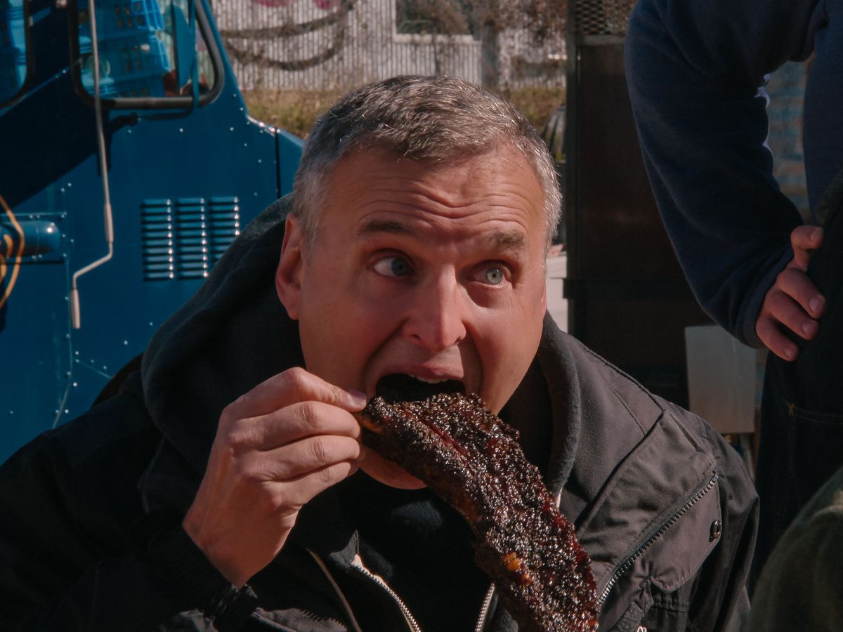A man in a coat eating a big rib.