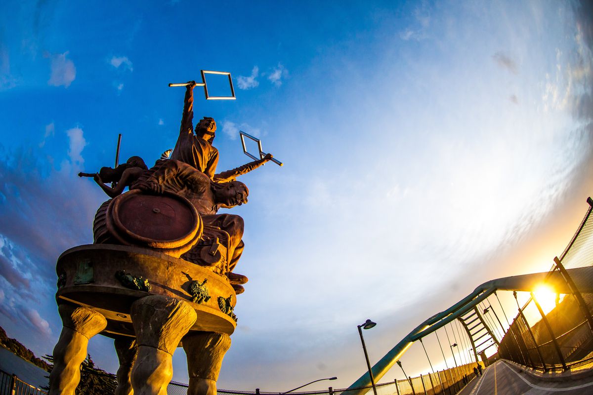 A blue sky highlights a massive reddish sculpture featuring characters protesting. 