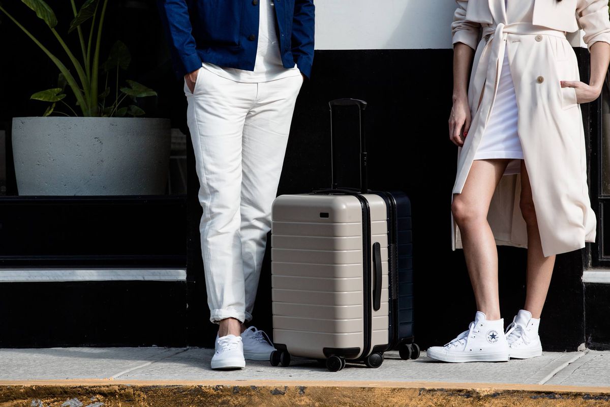 A man and a woman, shown from the waist down, standing near a carry on suitcase