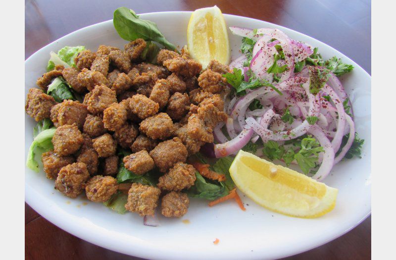A plate of fried liver cubes, with chopped red onions, herbs, and lemon wedges
