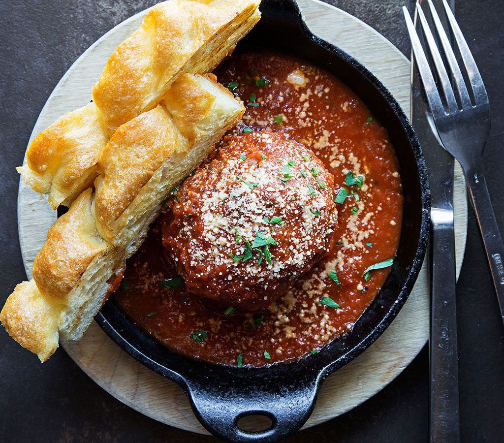 A huge meatball surrounded by marinara in a skillet