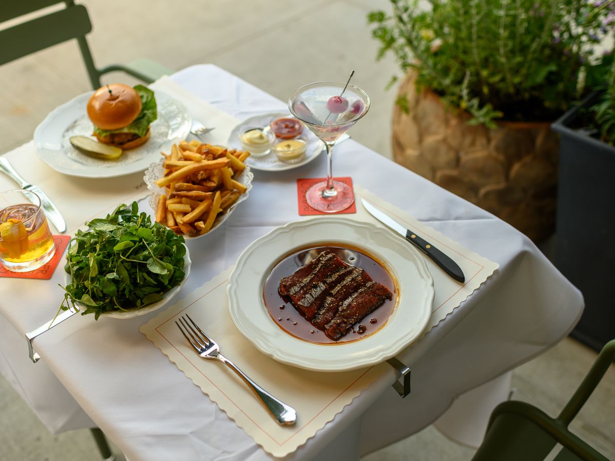 An outdoor table set with steak, fries, a burger, salad, and a martini.