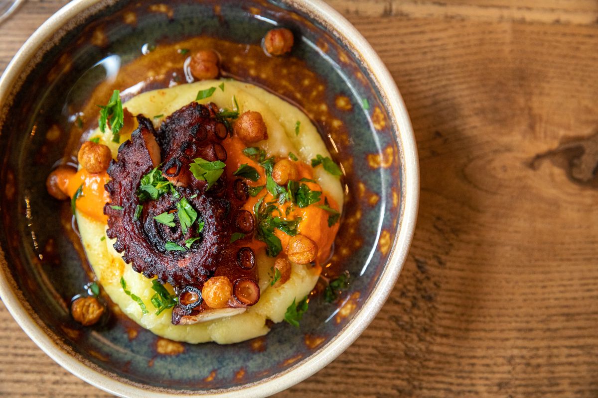 Octopus with potato puree, piquillo peppers, and chickpeas in a bowl.