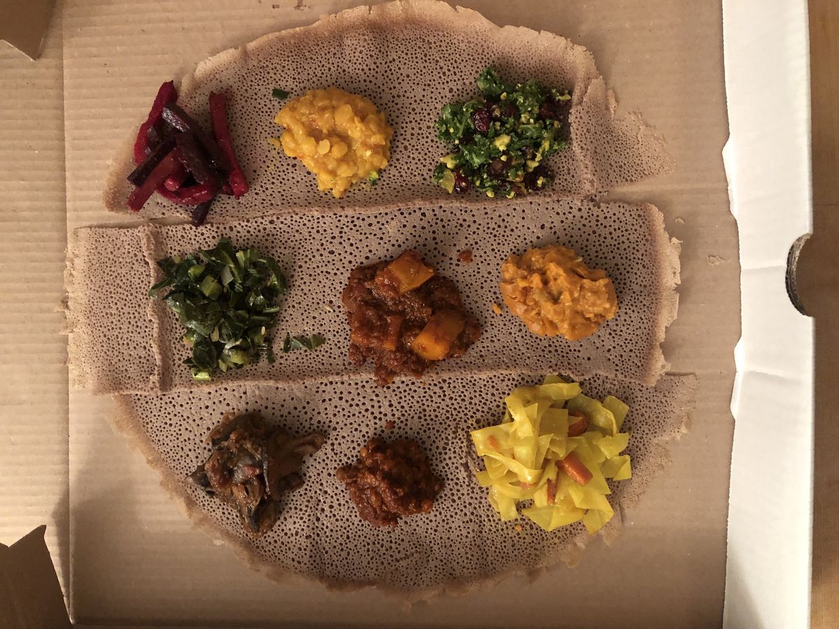 The interior of a pizza box with a circular brown injera rolled out and scoops of colorful veggie preparations placed on top.