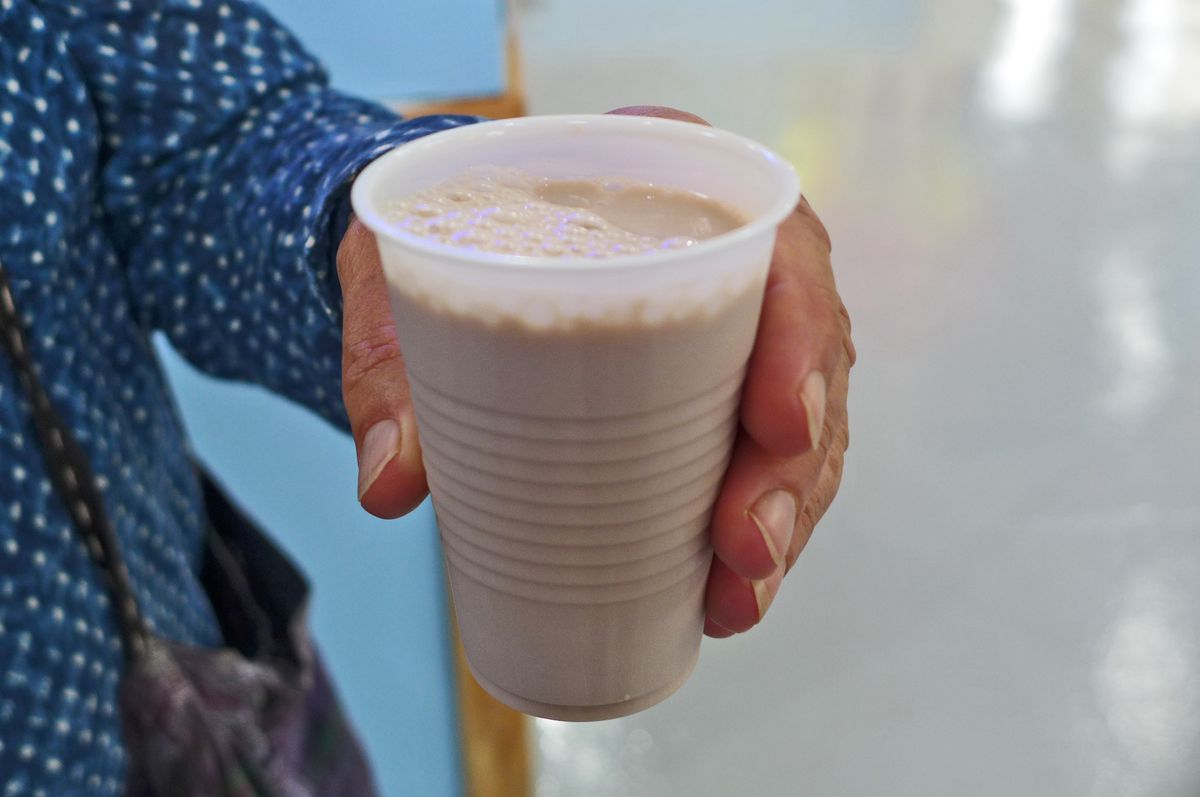 A hand holds a plastic glass of chocolate milk.