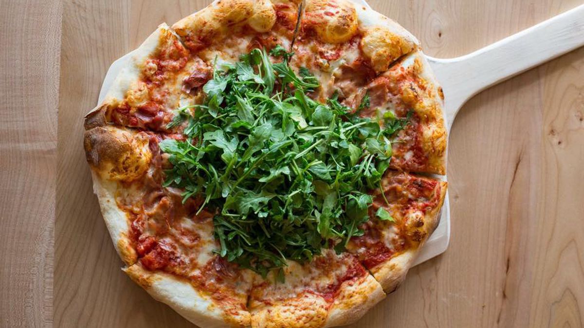 A pizza with vibrant greens, bubbling cheese, sauce, and a rustic crust sits on top of a peel.