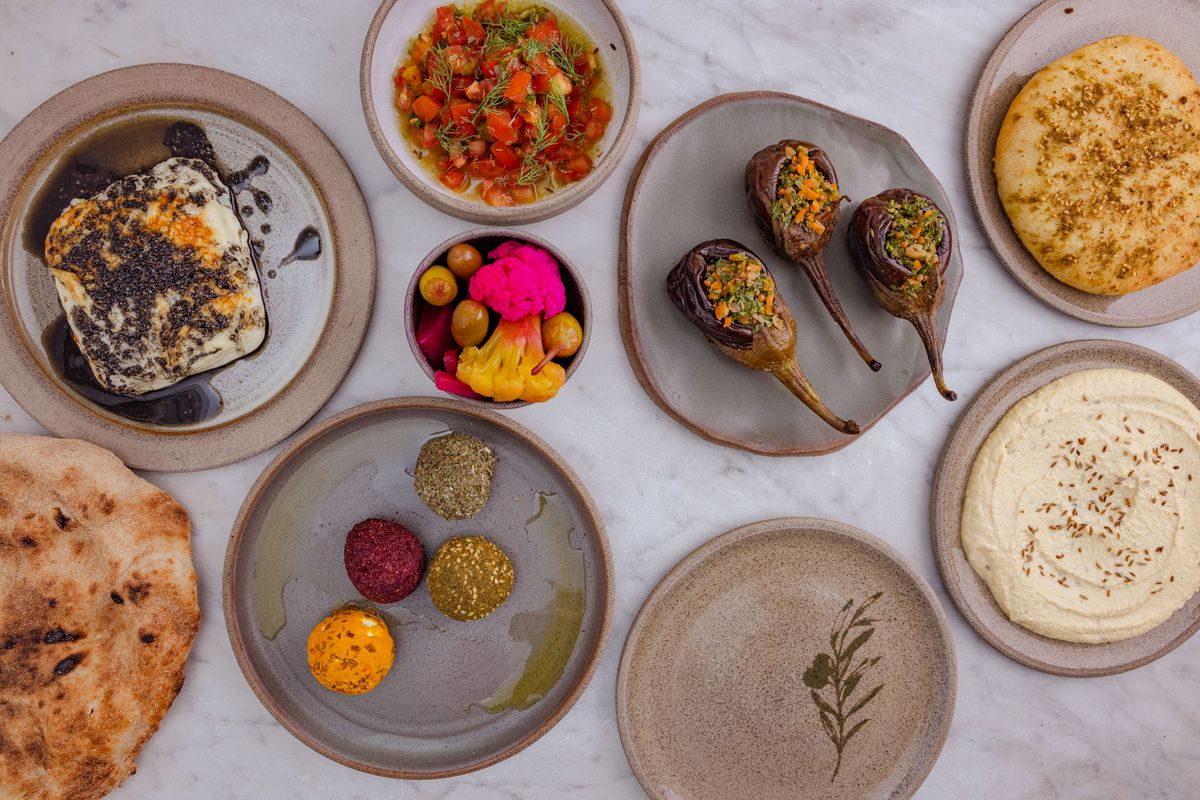 A birdseye view of pickles, breads, aubergines, tomatoes, cheese, and lentil balls on Palestinian ceramics.