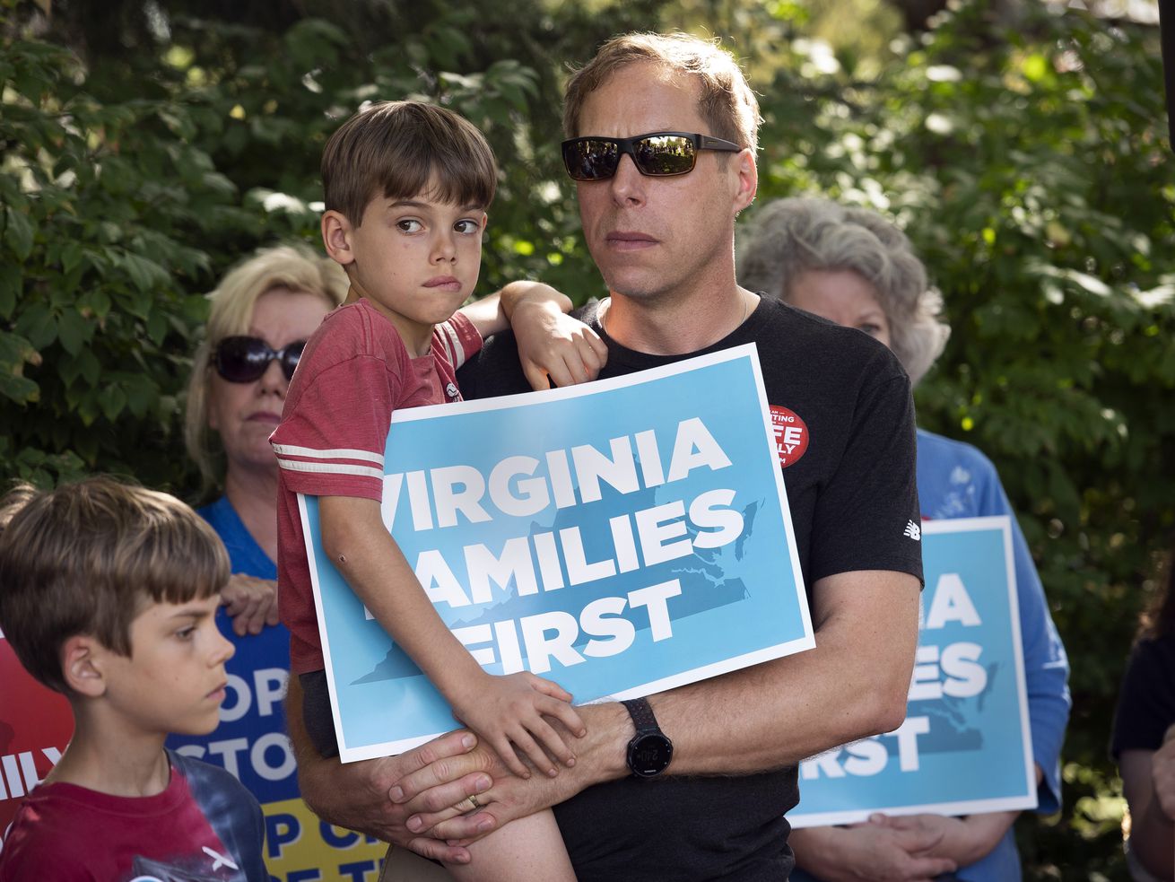 Patrick Novecosky holds son Daniel as son Peter stands beside them during a rally tied to the Virginia governor’s race.