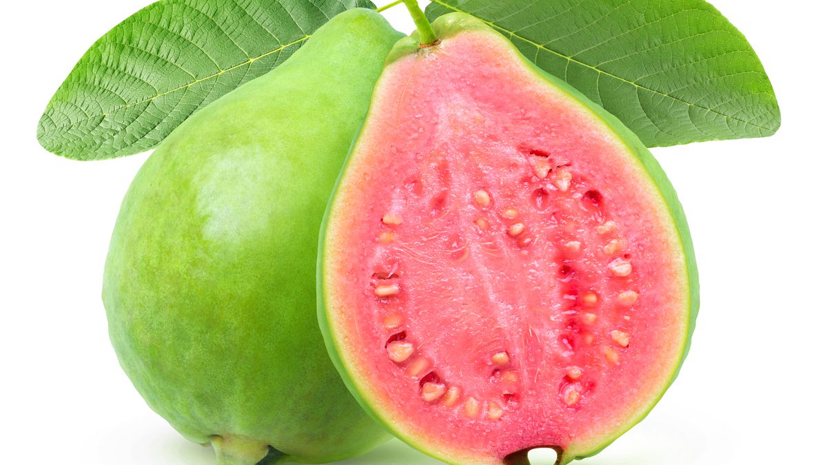 A green-skinned guava, sliced open to reveal a pink fleshy interior with white seeds, is isolated on a white background