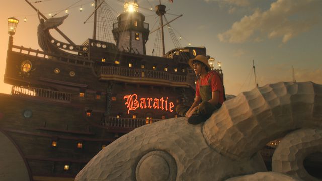Luffy (Iñaki Godoy) sits on the masthead of his ship in front of the Baratie sign