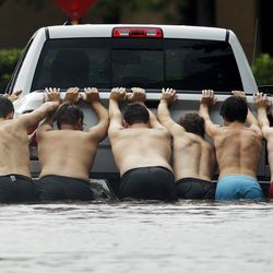 People push a stalled pickup through a flooded street in Houston, after Tropical Storm Harvey dumped heavy rains, Sunday, Aug. 27, 2017. The remnants of Harvey sent devastating floods pouring into Houston on Sunday as rising water chased thousands of people to rooftops or higher ground.
