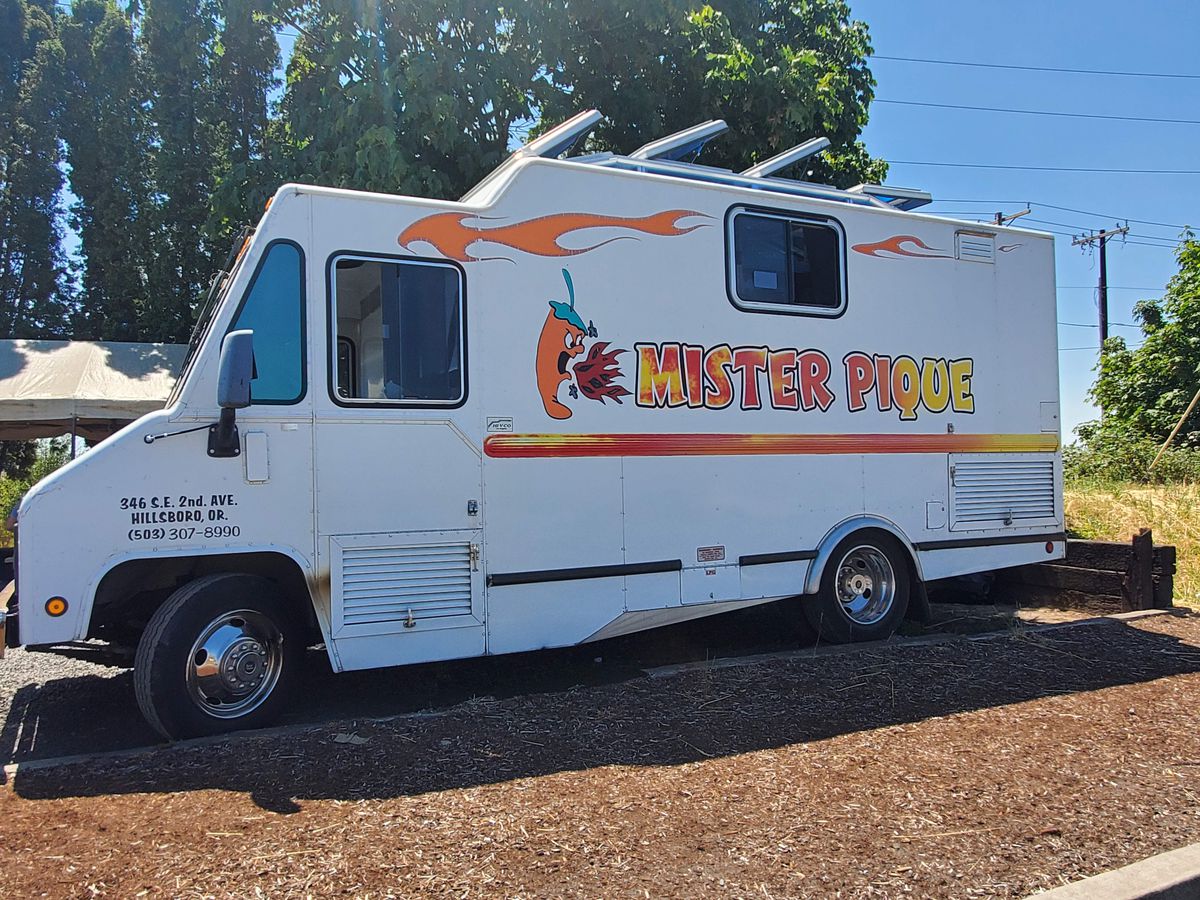 A white taco truck is seen with a blue sky and trees behind it.