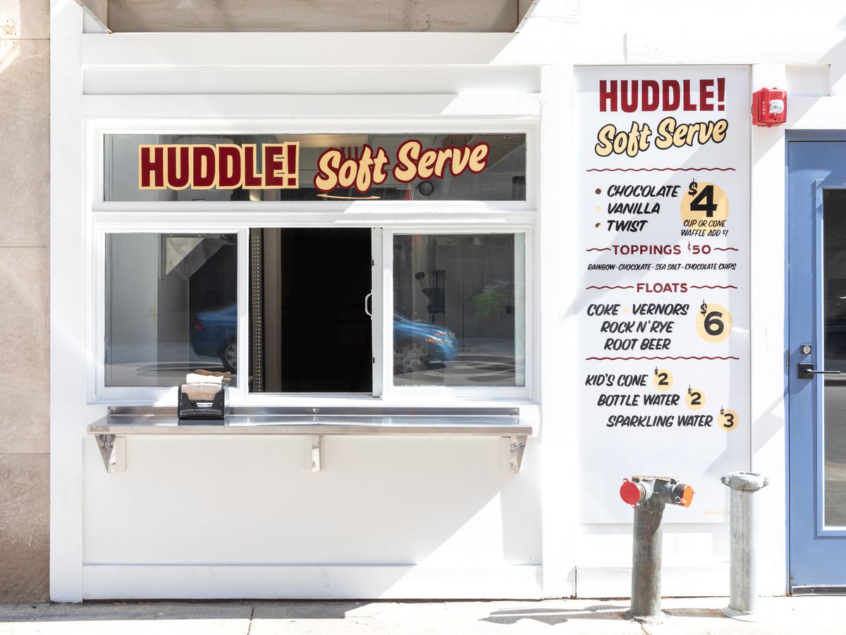 a white walk-up window for Huddle with red and yellow signs and menus