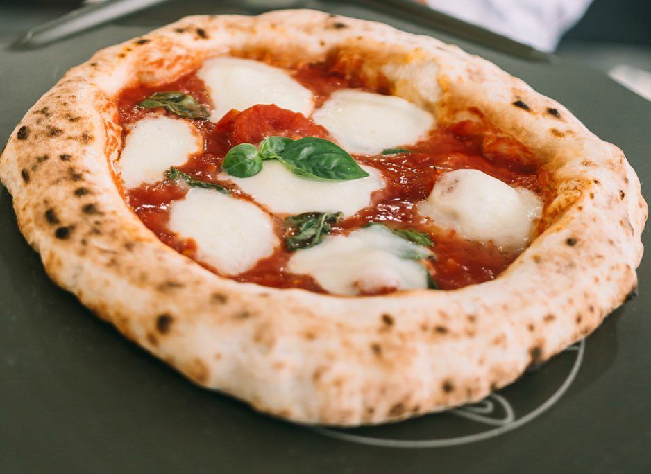 A full pizza with puffy crust around the edges, thick rounds of cheese, mountains and valleys of sauce and a few sprigs of basil