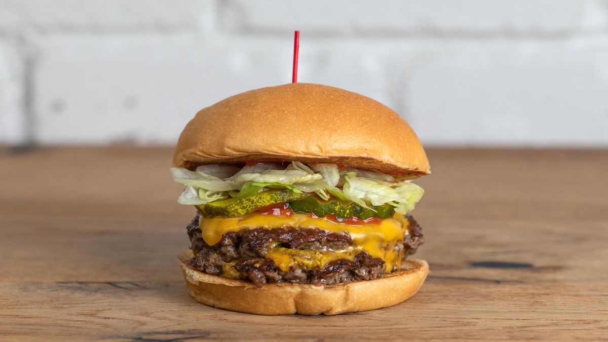 A double cheeseburger on a wooden table with lettuce on top.
