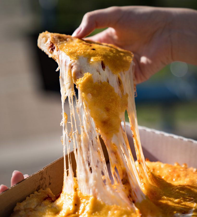 A hand pulls a slice of pizza from a pie in a box, trailing huge amounts of gooey cheese behind
