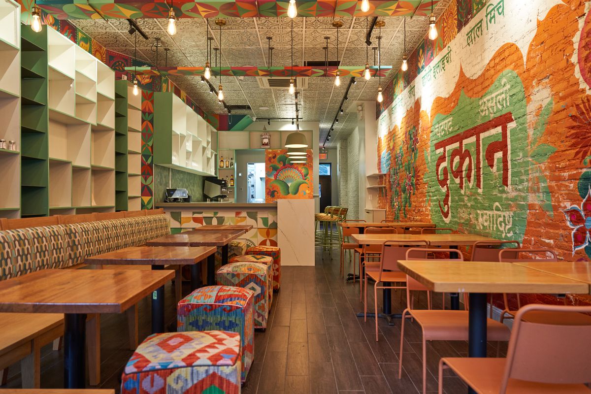 A bright dining room with wooden tables and patterned stools and brightly colored brick walls.