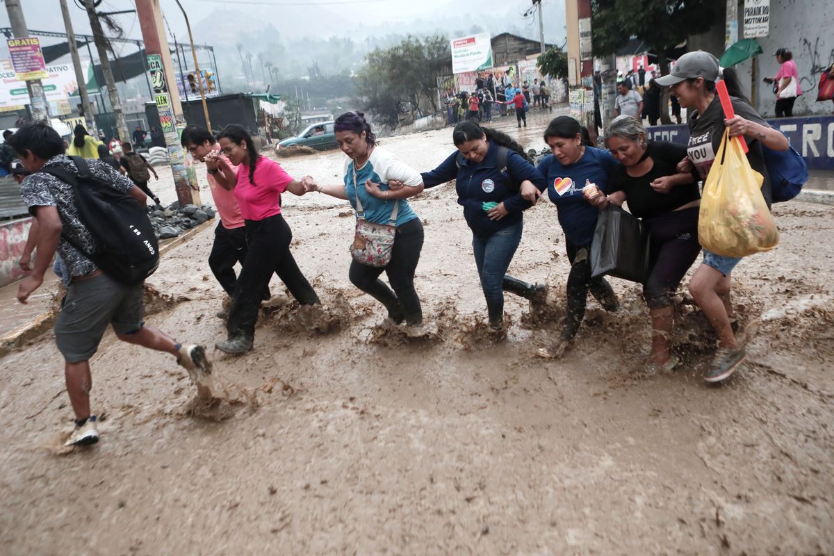 A group of people wade across a street arm-in-arm through a mudslide caused by heavy rains from Cyclone Yaku in the Chosica district on March 18, 2023.