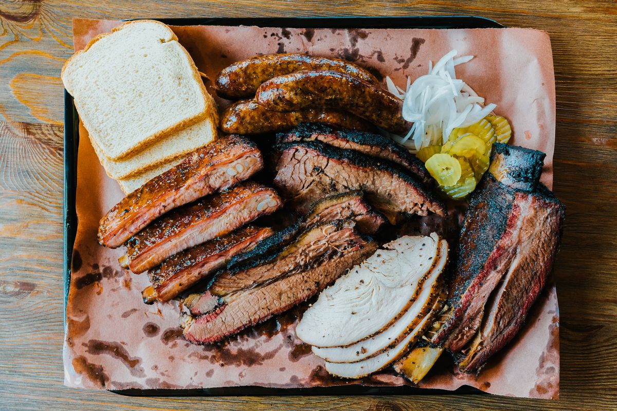 A tray of brisket, sausages, turkey, and bread and pickles