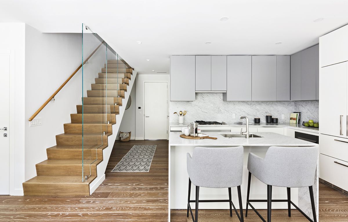 A wooden staircase covered in glass and a kitchen with grey cabinetry on its right side.