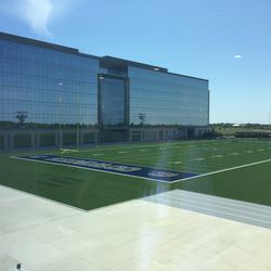 On the opposite side is a view of one of two practice fields. Here we see the ProTurf field; the other is made of grass. Jerry Jones’ office is in the middle of the first floor of the glass building we see here. Behind the far end zone is Jerry Jones’ private helipad.