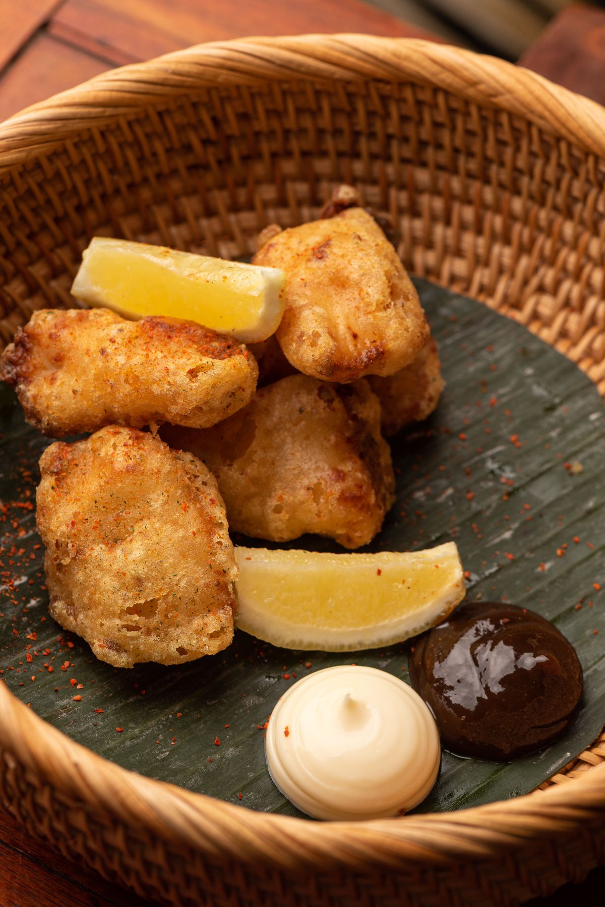 Mochiko chicken karaage nuggets with kewpie mayo and tonkatsu sauce over banana leaf in the wicker basket.