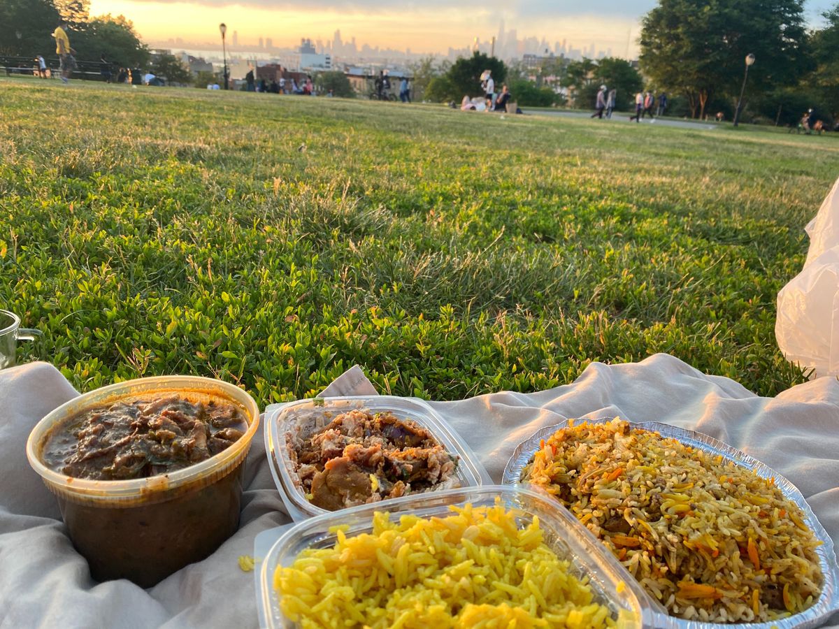 Cups of rice, chaat, goat nehari, and chicken dum biryani on a gray blanket set in the grass