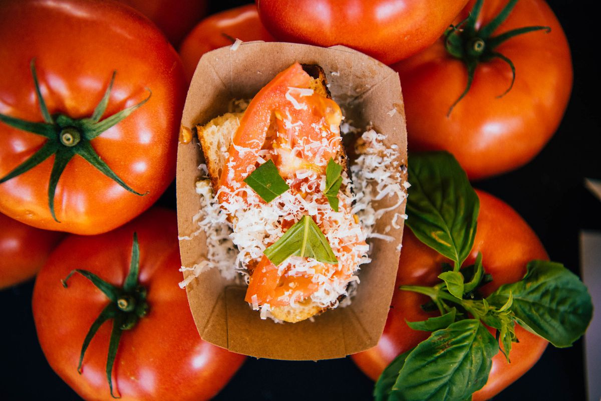 A cardboard tray of a tomato-topped dish on top of a pile of red tomatoes.