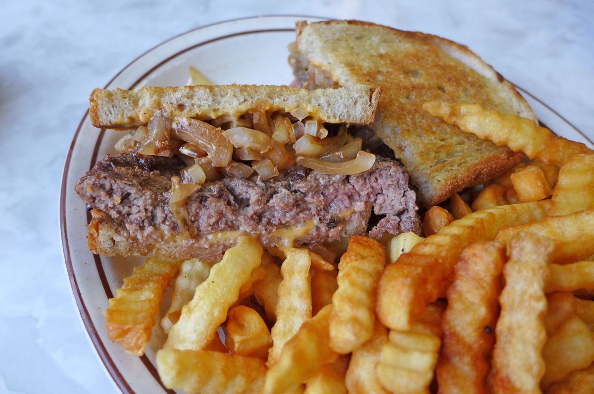 A burger in toast with crinkly fries.