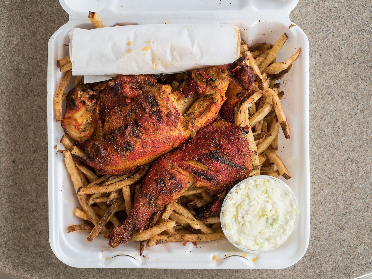 An overhead shot of red sauced grilled chicken atop fries in a takeout container.