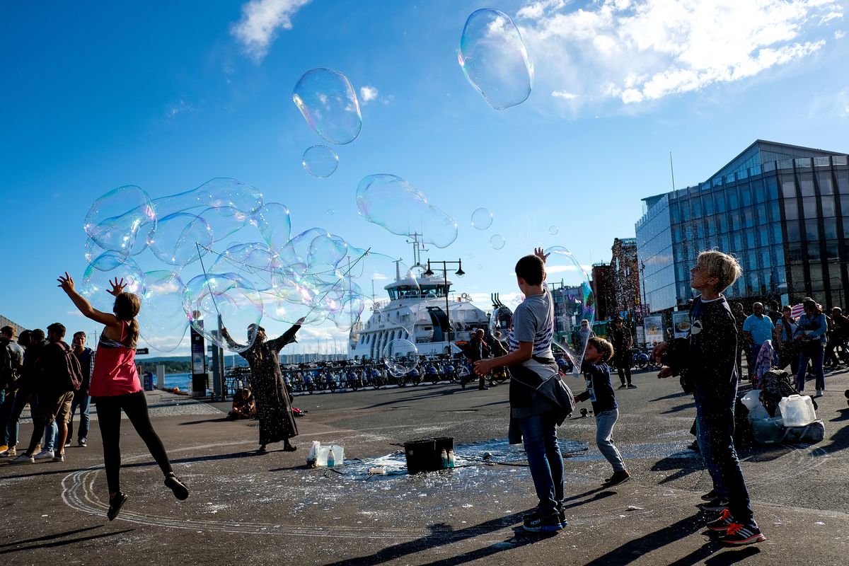 Children play as a man makes bubbles in the Aker Brygge harbor in Oslo, Norway, on Sunday, Aug. 12, 2018.