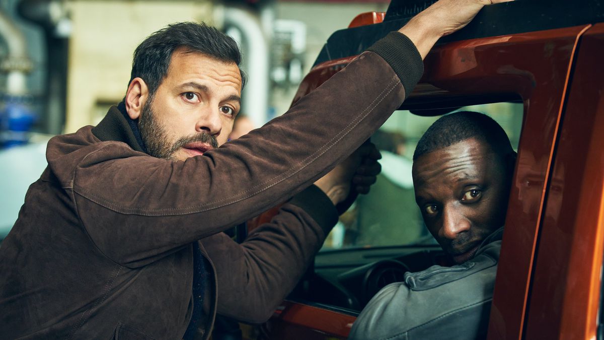 Laurent Lafitte (standing outside an orange vehicle) and Omar Sy (sitting in it) in The Takedown