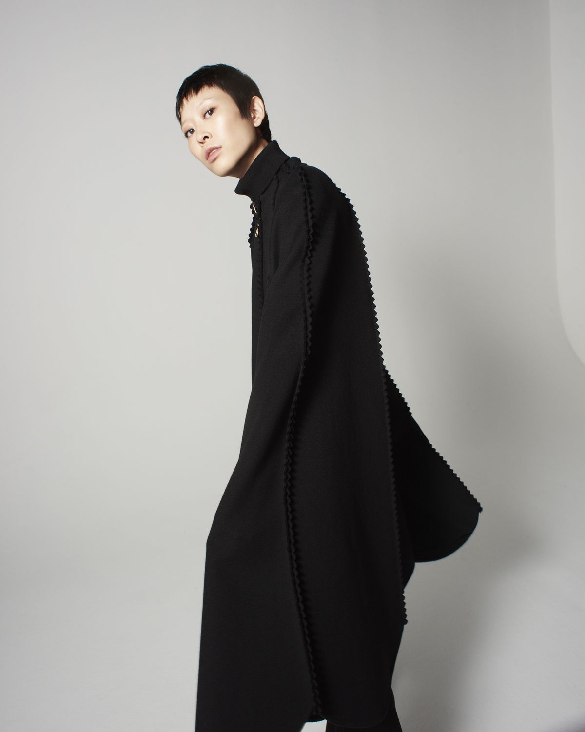 A model with short hair wearing a black cape