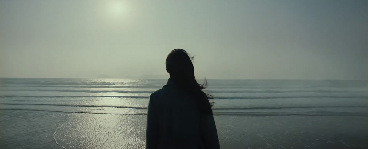 A woman with her back to the camera looks out over a peaceful ocean in Decision To Leave