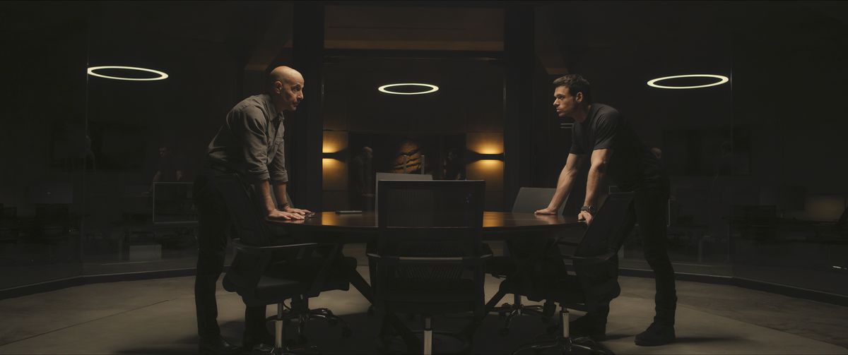 Bernard (Stanley Tucci) and Mason (Richard Madden) leaning over opposite ends of a table and looking at each other in a still from Citadel season 1