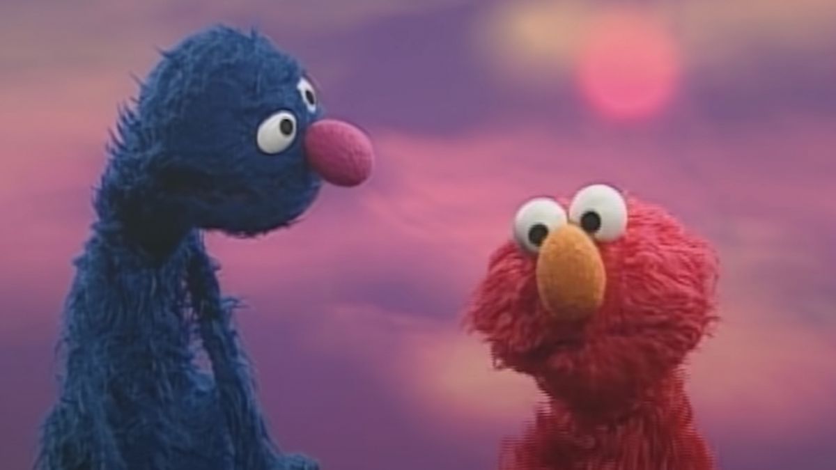 Grover stars and at Elmo during a song in Sesame Street in front of a sunset background.