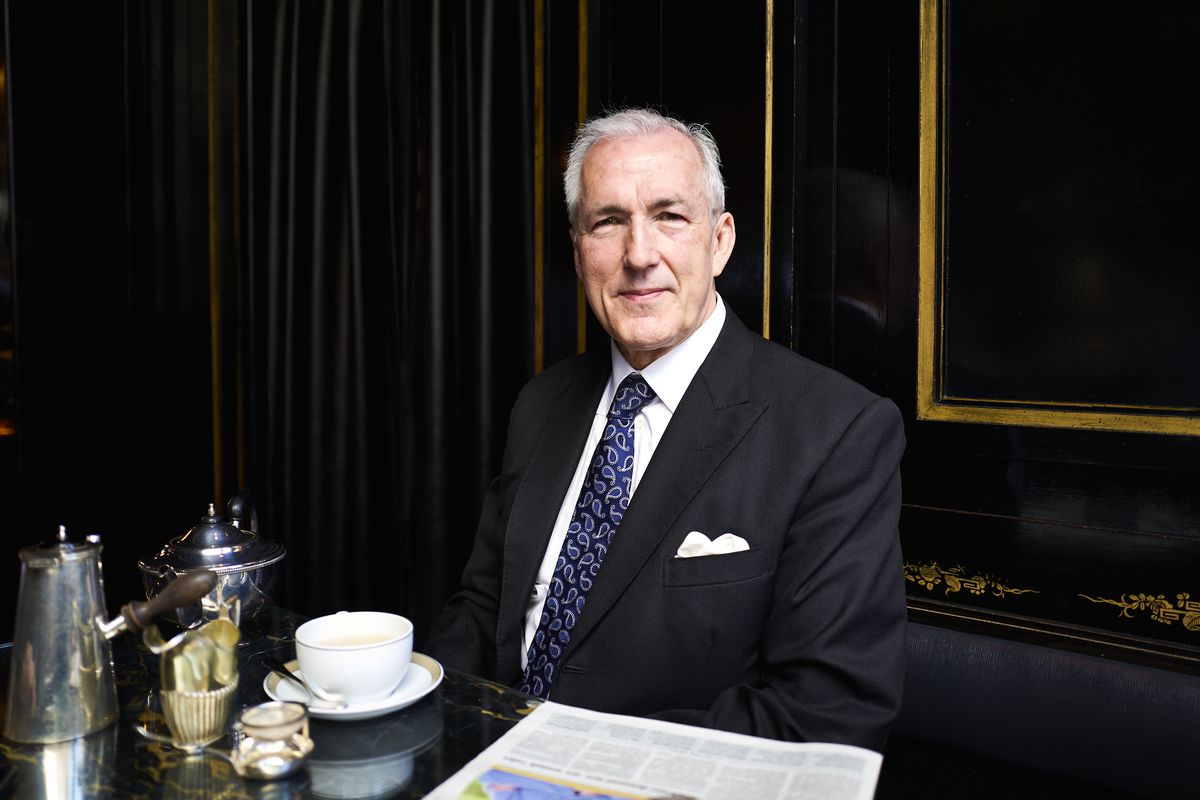 Jeremy King, wearing a suit and tie, sits in a black and gold booth with a tea set in front of him.