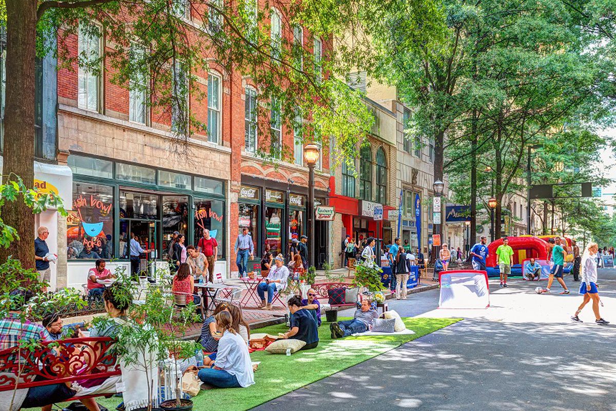 People sit and walk through the downtown’s Broad street, which is lined with retail buildings and greenery.