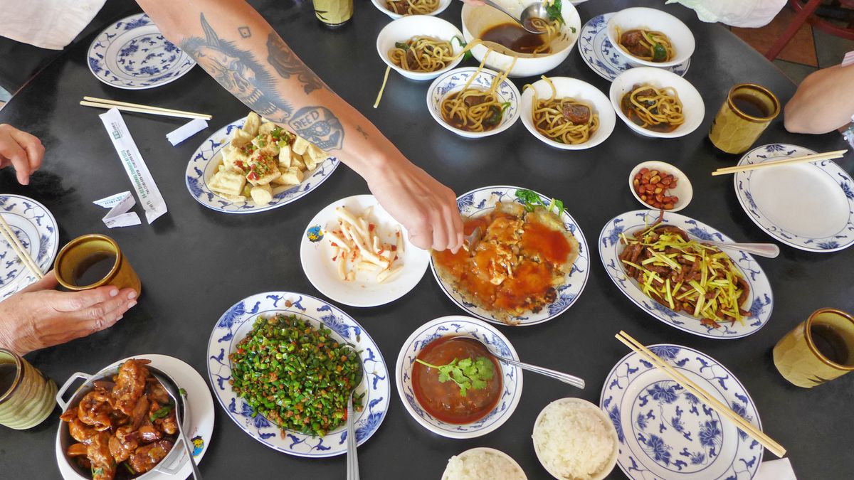 A tattooed arm reaches for an oyster omelet, with dishes all around seen from above.