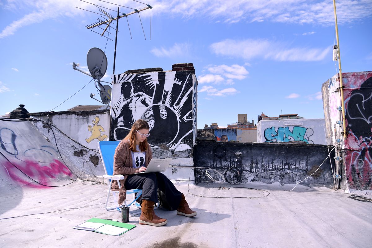 A woman uses a laptop on a roof in New York City.