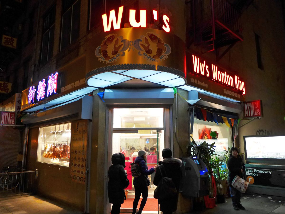 A corner restaurant has brightly lit, block font signs saying Wu’s Wonton King.