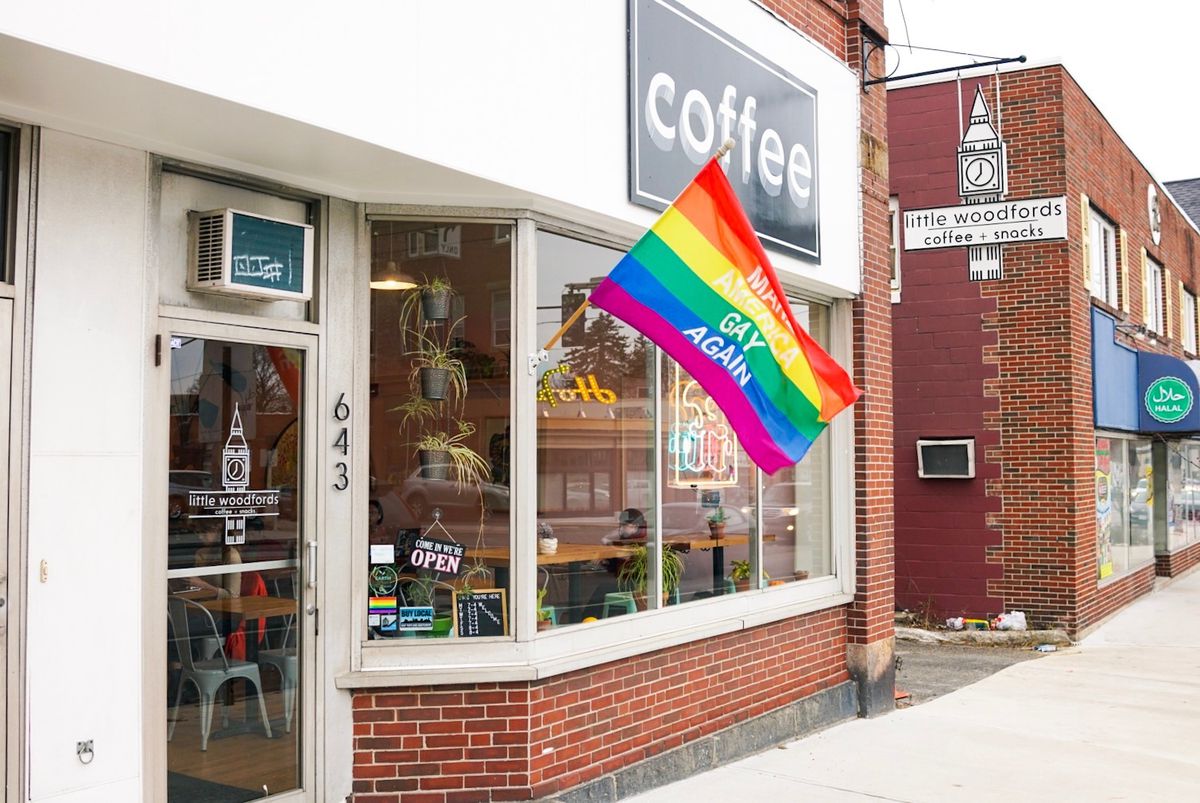 Exterior of a cafe with a large black sign with white lettering that reads “coffee.” A rainbow flag flies outside of the cafe with the words “Make America Gay Again.”