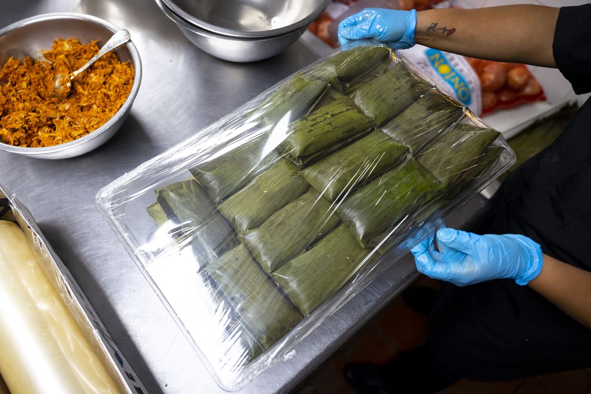 Oaxaoueños tamales wrapped in banana leaves under plastic on a tray.