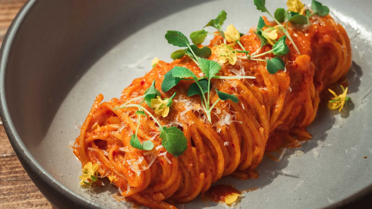 Closeup shot of a portion of spaghetti rolled up in a thick bundle down the middle of a gray plate. It’s in a tomato sauce and topped with microgreens.