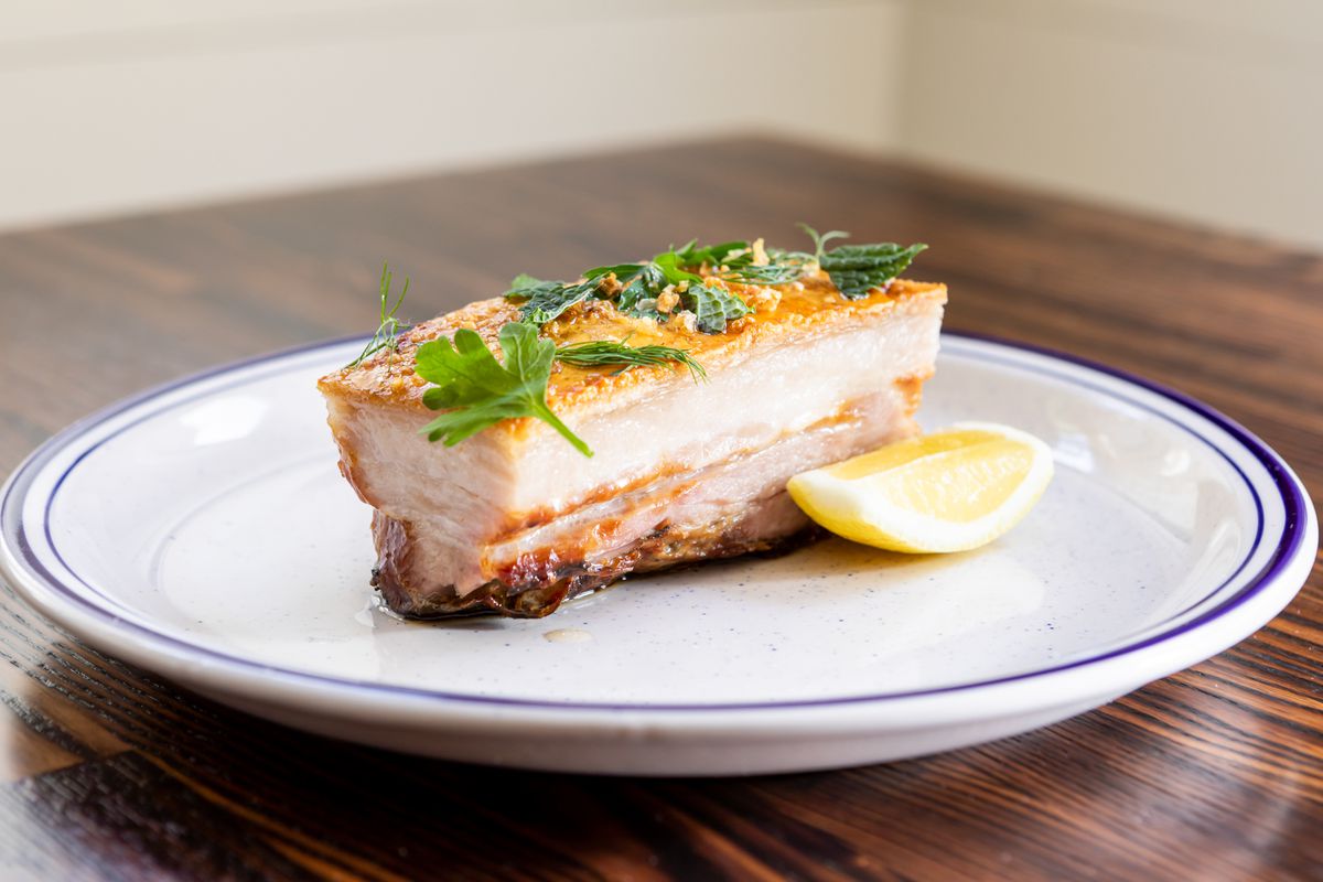 Crispy pork belly on a plate with herbs and lemon