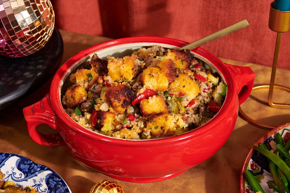 Bowl of cornbread stuffing in a red serving bowl with gold spoon.