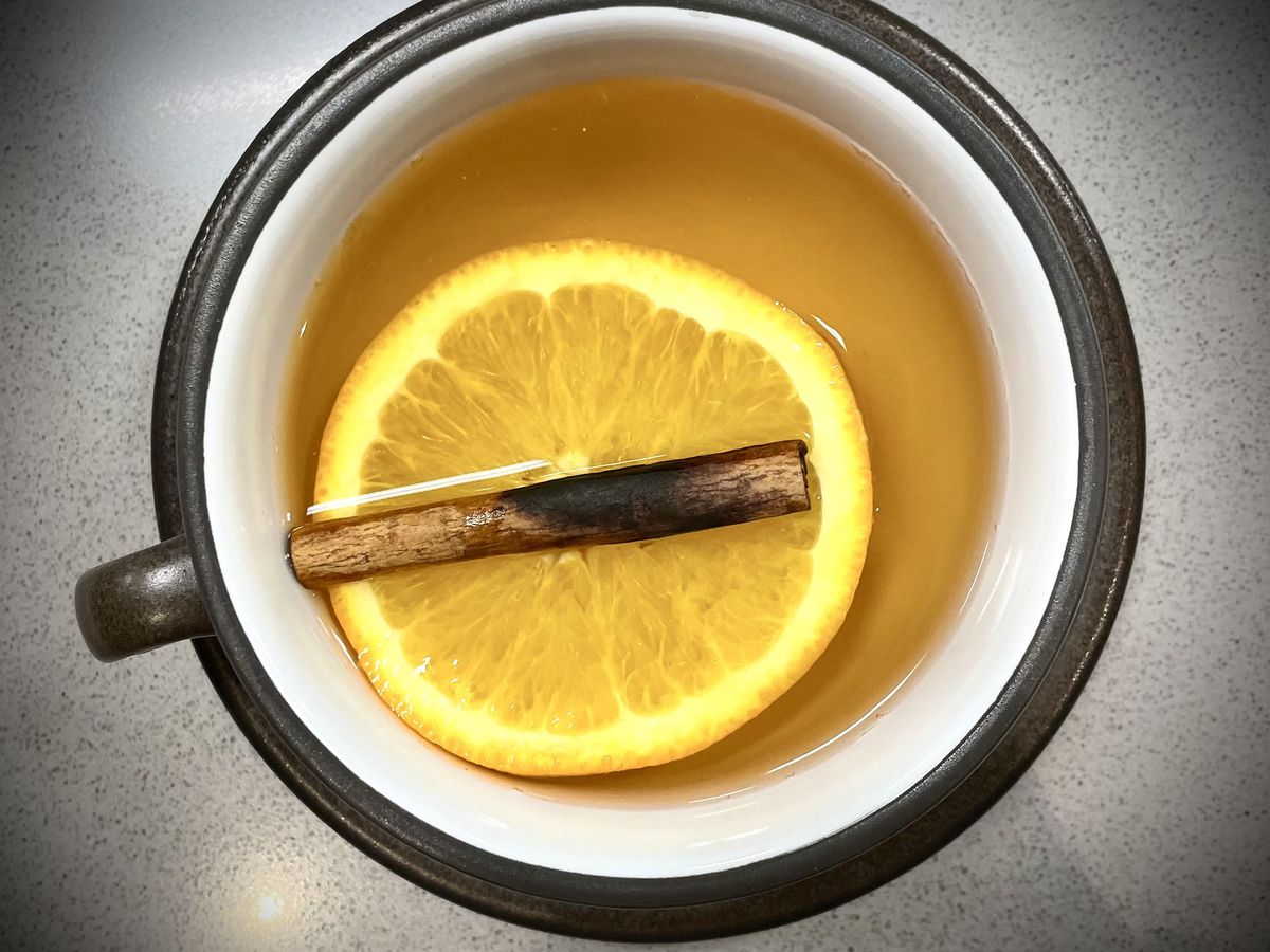 An aerial shot of hard apple cider in a mug with a floating cinnamon sprig and lemon.